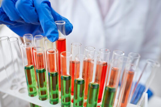 gloved hand holding a laboratory glass test tube filled with red end green liquid